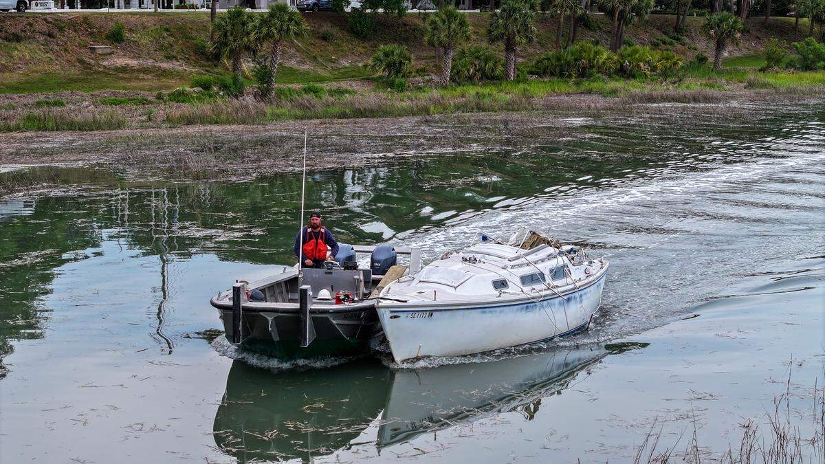 A worker with O’Quinn Marine brings a small boat back to the barge for removal after it was pulled from the bank of the Beaufort River on the evening of April 23, 2025 in Historic Beaufort. The company has been hired to remove five beached boats after they were ripped from their moorings during Tropical Storm Helene in 2024.