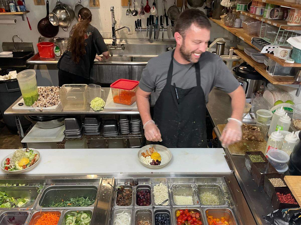 Delisheeyo owner Blake Wearren shares a laugh with an off-camera employee as he assembles salads at his Hilton Head restaurant. Beneath his upbeat demeanor, Wearren is still processing the shock of losing almost everything he owns to a house fire. 