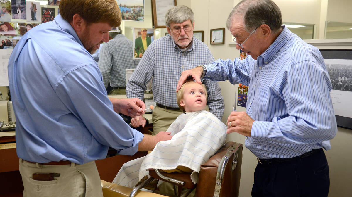 Michael Youmans, left, and David Youmans, watch as James Youmans, center, 1 year old, looks up at barber Ray Harvey, right, as he gets his first haircut Nov. 19, 2014, at Harvey's Barbershop in Beaufort. David has been getting his hair cut by Ray for the past 50 years, his son Michael got his first haircut by Ray and has been coming back ever since and now James is the third generation to get his hair cut by Ray.