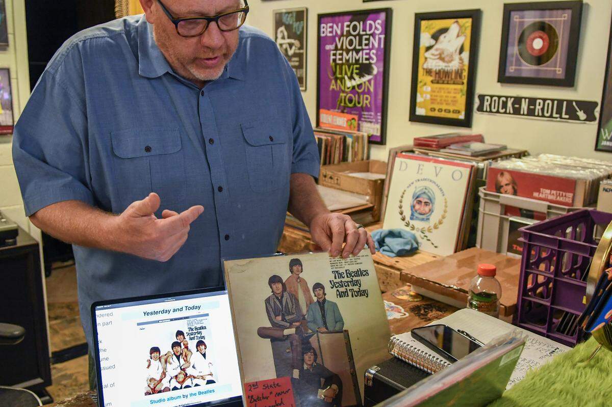 Josh Duvall, co-owner of MoJo’s Island Records, explains on April 7, 2025, about The Beatles “Yesterday and Today” album cover that was pulled from the shelves in the 1960s in the United States. The original image on the sleeve was photographed by Robert Whitaker, left, and dubbed the “butcher cover.” Members of the band wore butcher smocks with raw meat and doll parts. Instead of destroying the albums, the record company covered the album with a sticker of the band, shot by the same photographer, right, that is for sale at the Palmetto Bay Road store on Hilton Head Island.
