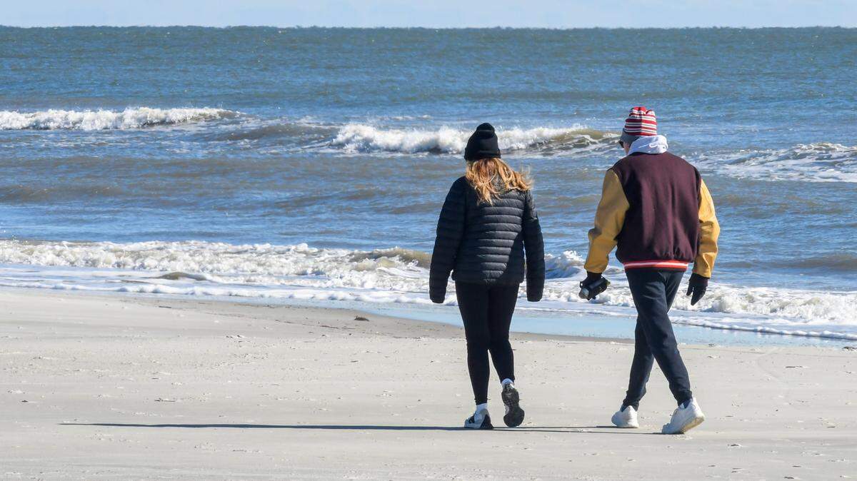 A couple wearing winter coats, hats and gloves walks along the beach near Coligny Beach Park with a stiff breeze off the Atlantic Ocean on the frigid morning of Tuesday, Jan. 7, 2025, on Hilton Head Island. For the first weeks of the new year a polar vortex from the high Arctic will bring freezing temperatures to parts of the deep south.