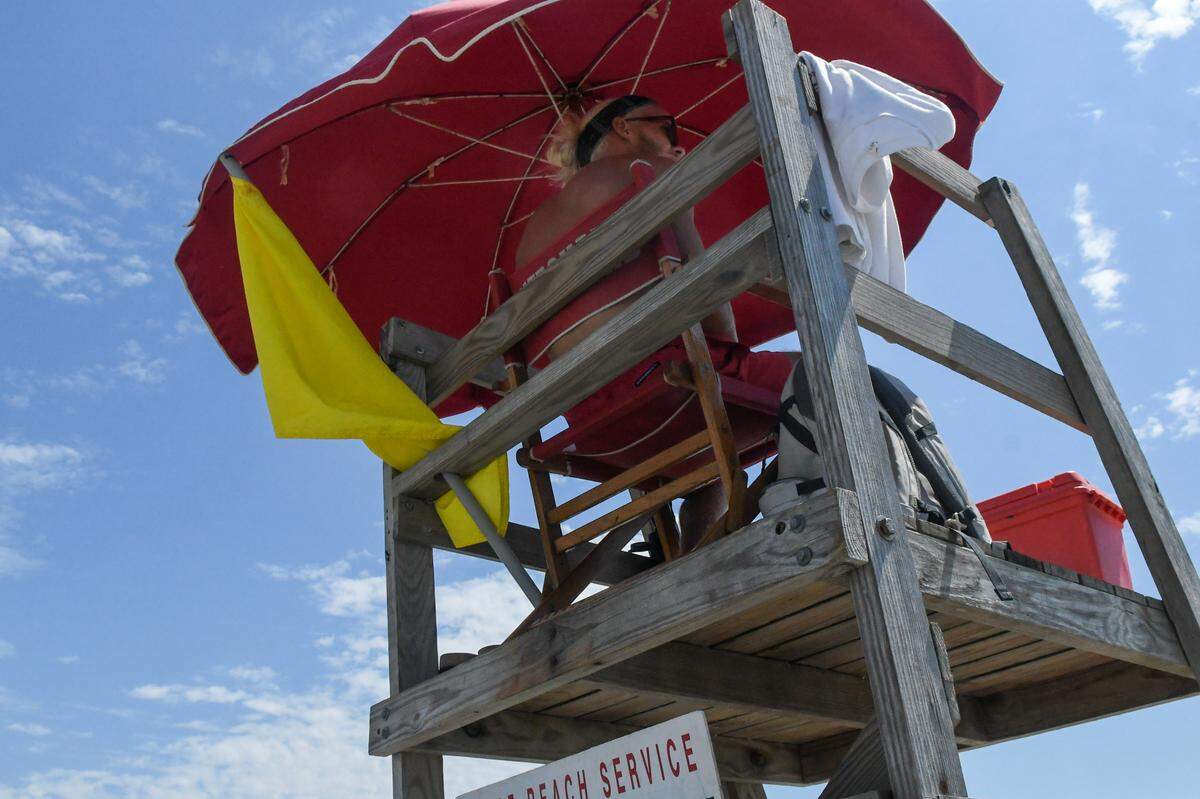A Shore Beach Service lifeguard displays a yellow flag that warns beachgoers of stronger than usual surf.