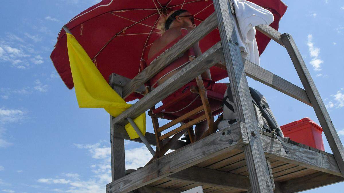 A Shore Beach Service lifeguard displays a yellow flag that warns beach goers of stronger than usual surf, including rip currents.