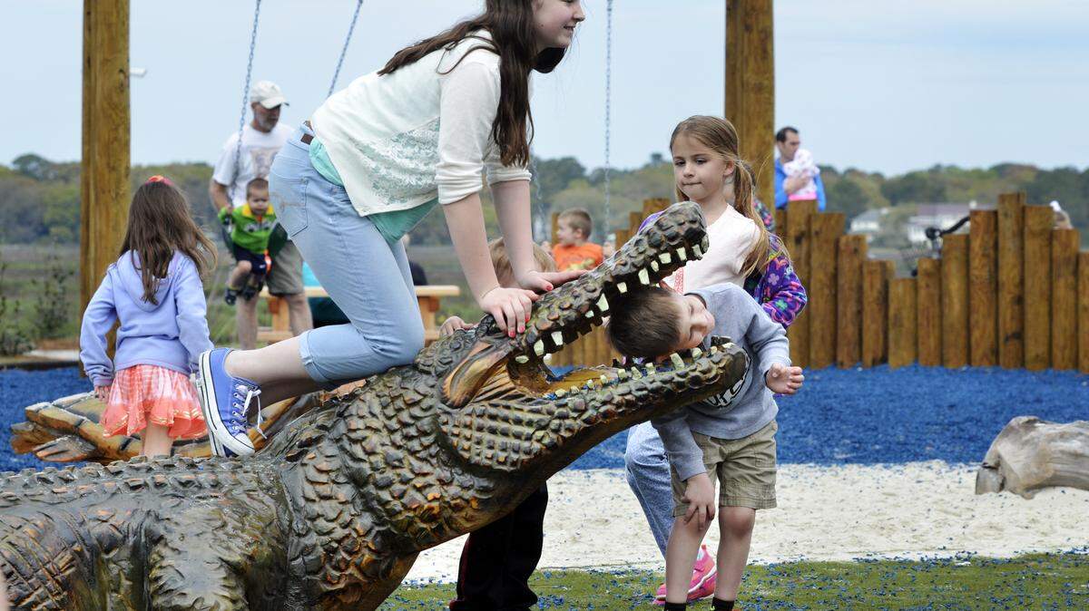 Ava Schloss, of Ohio, left, kneels on top of an alligator sculpture as her brother Augustine Schloss, right, rests his head inside of the mouth of the alligator while posing for a photo at  Shelter Cove Community Park on April 1, 2015.
