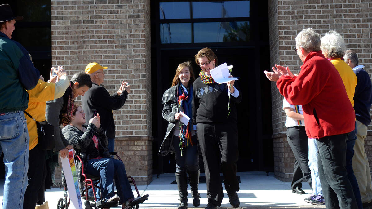 Alayna Reynolds, 21, center left, and Michael Raye Lutz, 28, center right, who identifies as transgender, walk out of the Beaufort County Courthouse to applause from members of the Unitarian Universalist Fellowship of Beaufort after applying for their marriage license on Thursday afternoon.  Reynolds and Lutz, both of Hilton Head Island, are the first same-sex couple to apply for a marriage license in Beaufort County.