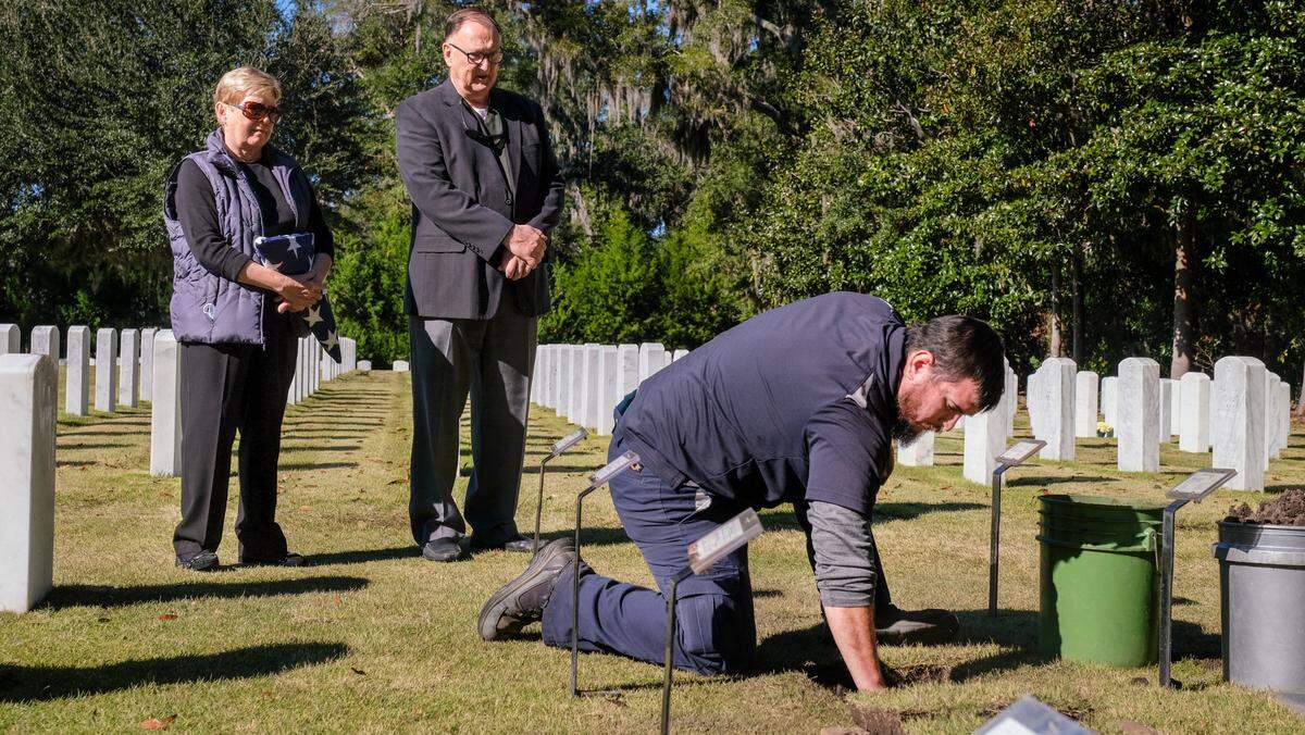 Alex Garcia, front, a Beaufort National Cemetery caretaker gently places the cremation remains of WWII veterans Charles B. Read Sr. and Valerie L. Read, parents to Charles Read Jr., center, and in-laws to his wife, Alice Read into the earth on Tuesday, Nov. 9, 2021, at the historic cemetery. After keeping his parents ashes for 20 years, Read said, minus the tears, “this is a happy event.” adding, with a sigh of relief, that the veterans are now at a “spot they’ll be forever.”