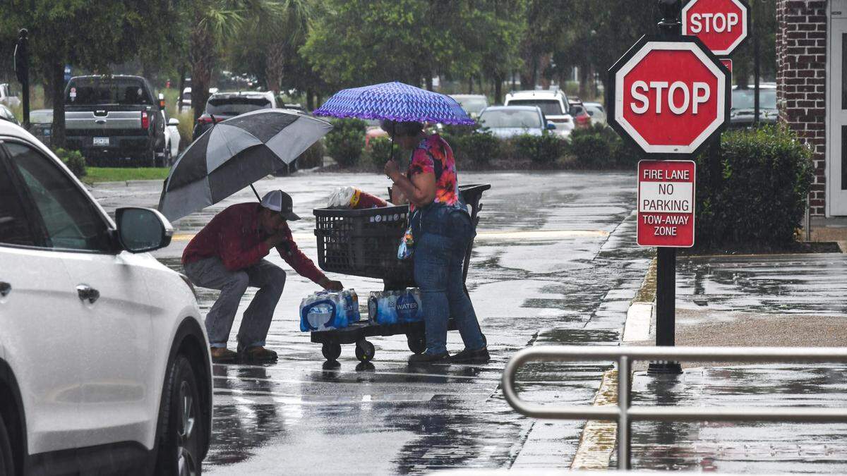 With rain pelting from Tropical Storm Debby, a man stop to help a woman put her water back onto her cart on Aug. 5, 2024 at Belfair Towne Village in Bluffton.