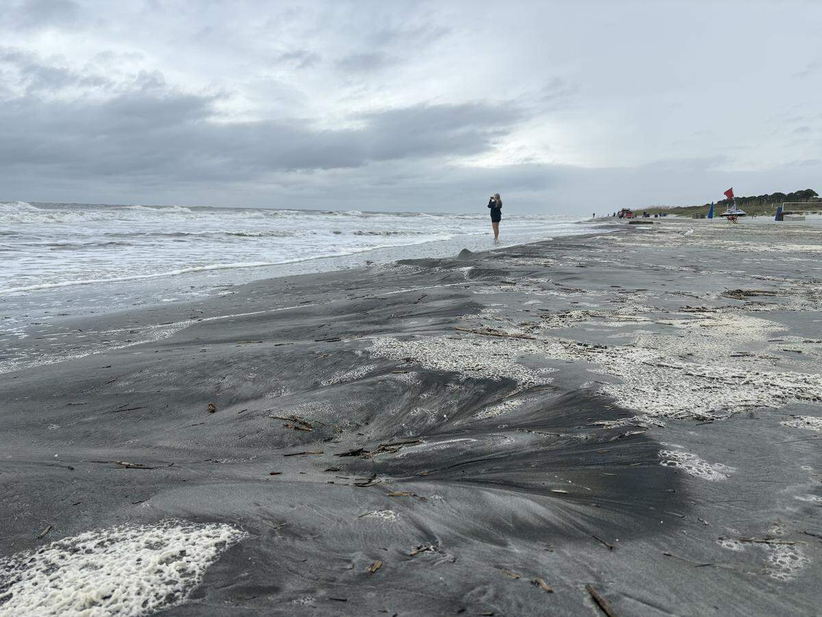 A woman takes a picture on the beach during a grey, stormy day.