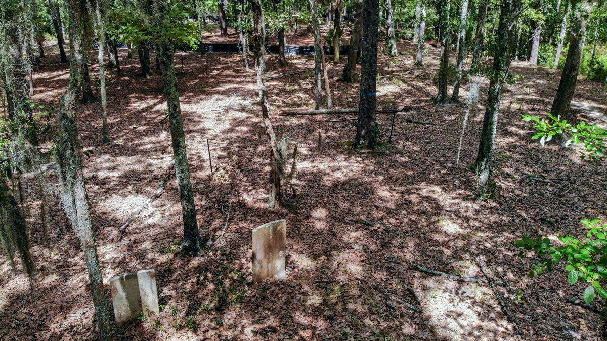 Black silt fencing, top, outlines the footprint of a future 5,735-square-foot home as dappled sunlight reaches two visible headstones, bottom, on land historically known as Cedar Point Cemetery as photographed on Thursday, July 27, 2023, near Callawassie Island. With several headstones dating back to the American Revolution, residential construction has been stopped until the land is searched for other graves that might be unmarked.
