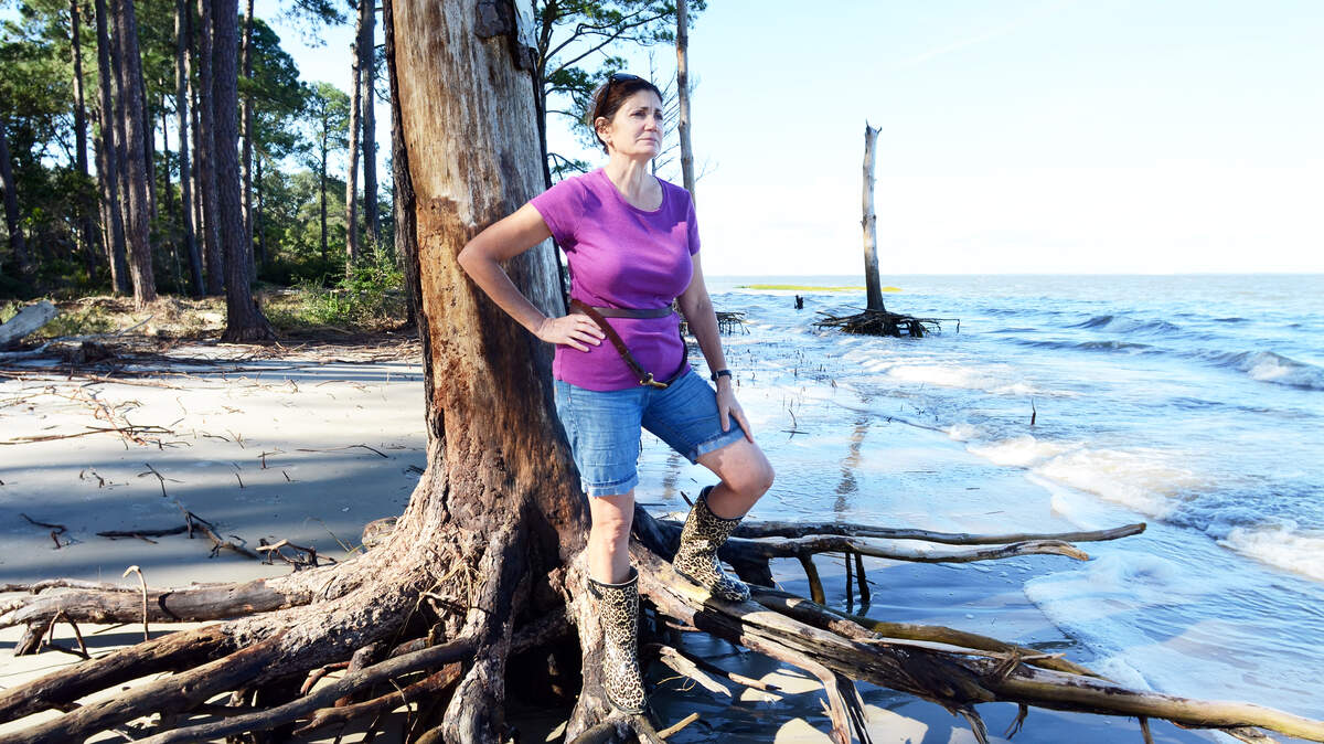 St. Helena Island resident Sandy Schepis stands on the exposed roots of a tree in her neighbor's yard along McTeer Drive as the high tide rises around it on Thursday. Last week's storm tides left a sandy beach where a grassy lawn used to be her yard, visible in background.