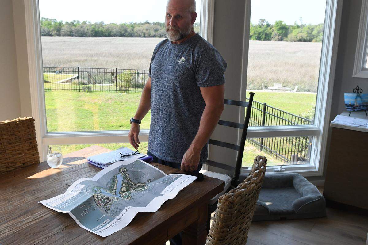 Cat Island resident Randy Mikals stands at his table on April 16, 2025, with a preliminary drawing of the proposed build out of Lower Cane Island, the island’s current natural beauty as a backdrop behind him at his Beaufort County island home. Mikals said he is concerned about the environmental impact of the project and the lack of infrastructure to handle 240 residential units and 130,000-square feet of commercial space.