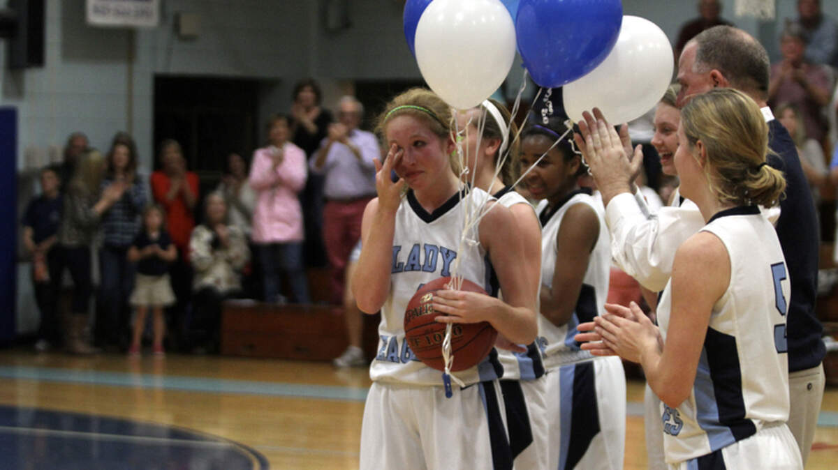 Beaufort Academy's Miranda Weslake (4), left, wipes away a tear as she is congratulated by her teammates after scoring her 1,000th career point during Friday's game with Thomas Heyward Academy.