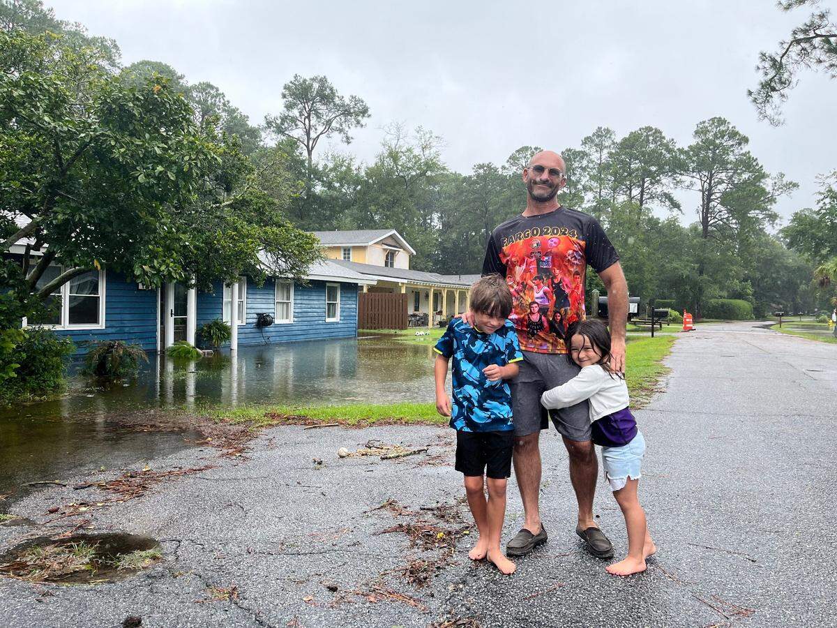 Michael Miller and his two children walk on Bay Pines Drive on Hilton Head Island, South Carolina, Tuesday, Aug. 6, 2024. His house isn’t flooded, but the people in home they’re standing in front of evacuated yesterday. “Our home is sitting up higher than these guys,” Miller said.