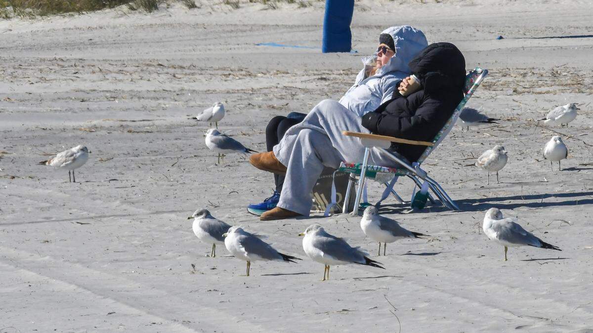 A bundled duo huddled together in beach chairs enjoys the warmth of the sun as a stiff breeze comes off the Atlantic Ocean on the frigid morning of Tuesday, Jan. 7, 2025 on Hilton Head Island. For the first weeks of the new year a polar vortex from the high Arctic will bring freezing temperatures to parts of the deep south.