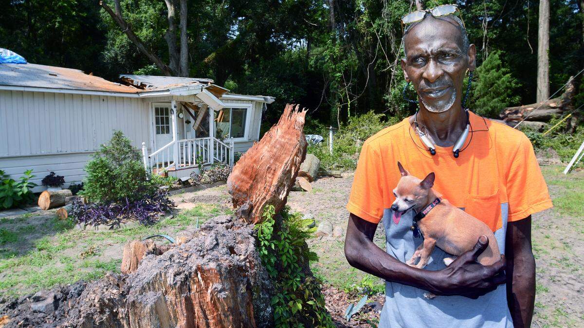 Beaufort resident Raymond Paige holds his dog, Trouble, on Wednesday as he stands next to the stump of the laurel oak tree that fell across his house late last week. Paige, a U.S. Army veteran and a retired civilian employee of Marine Corps Recruit Depot Parris Island, had said earlier that he couldn\'t afford to remove the tree. It remained atop Paige's house until Wednesday morning, when a workers from Lather Construction came by and volunteered their time and equipment to remove it.