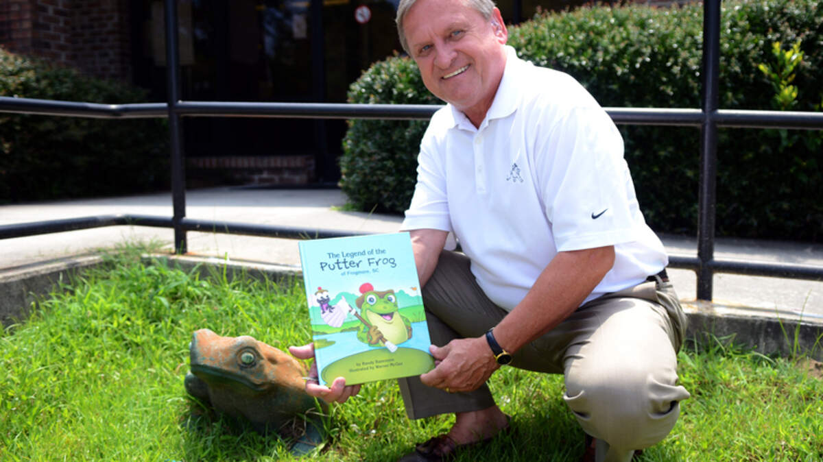 Beaufort's Randy Bazemore poses with the concrete frog that sits outside the St. Helena Island Post Office on Sea Island Parkway with his book, "The Legend of the Putter Frog of Frogmore, SC."