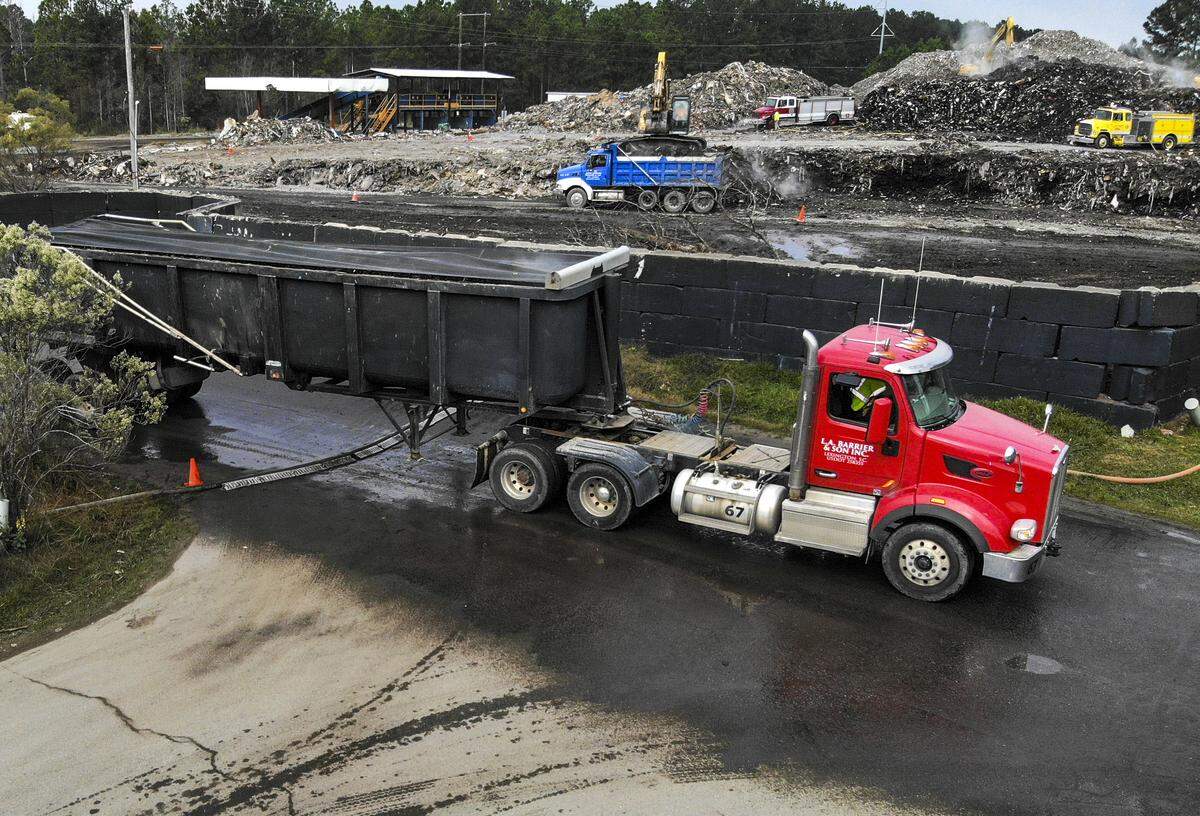 A dump trailer, front, leaves Able Contracting’s Material Recovery Center on Thursday morning as workers continue to remove debris at the Jasper County facility. The S.C. Department of Health and Environmental Control, now the lead agency, is using the larger trailers in tandem with tri-axle dump trucks, background, and hope to have the site free of debris by the end of the year.