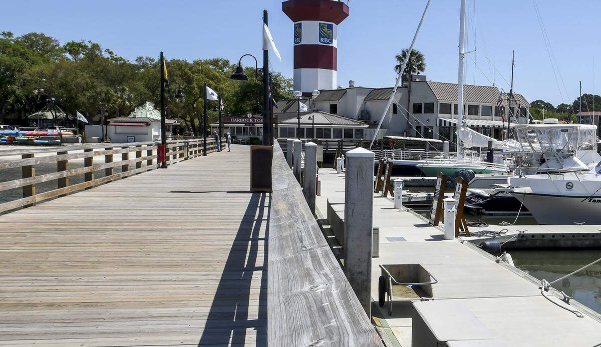Two people peer of the edge of the Harbour Town Boardwalk on Thursday, April 2, 2020, as kayaks and rental boats and personal watercraft sit idle near the yacht basin. The coronavirus has placed the economy on Hilton Head Island and around the world in a mode of silence.