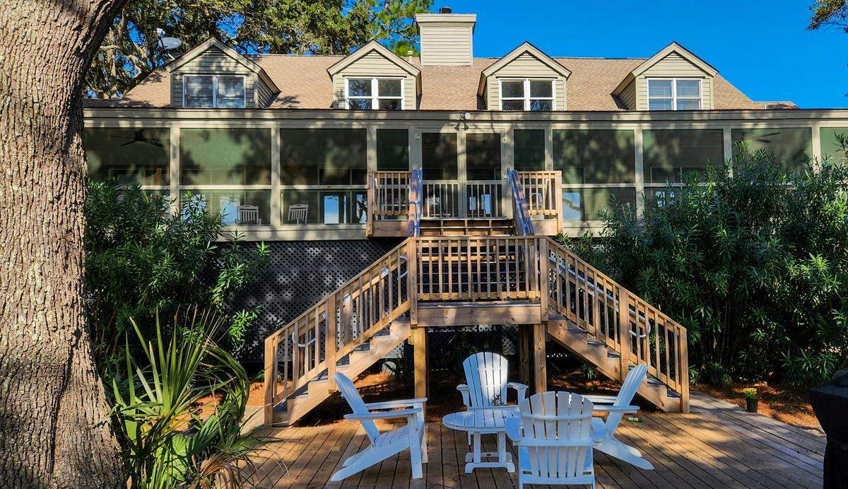 A full width screened porch of Ted Turner’s former St. Phillips Island home faces the ocean with stairs leading to a deck with a grill.