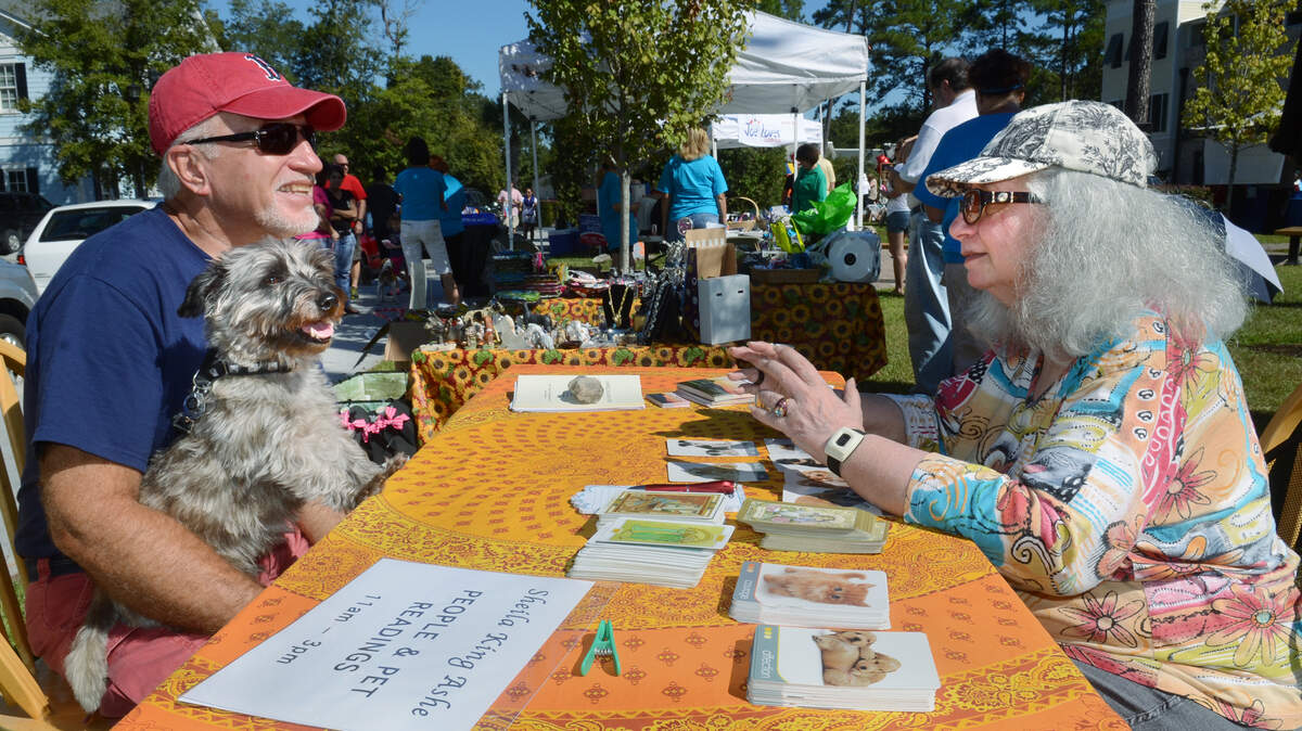 File: Spiritual Communications Consultant Sheila King Ashe, of Hilton Head Island, uses tarot cards to read the fortune of Digby the dog, held by owner Bill DeVries of Bluffton, during The Friends of Bluffton Dog Parks annual Bark in the Park fundraiser on Oct. 12, 2013, at the Calhoun Street Promenade. "I know he needs to change his treats," she said of Digby, who she pronounced otherwise fine.