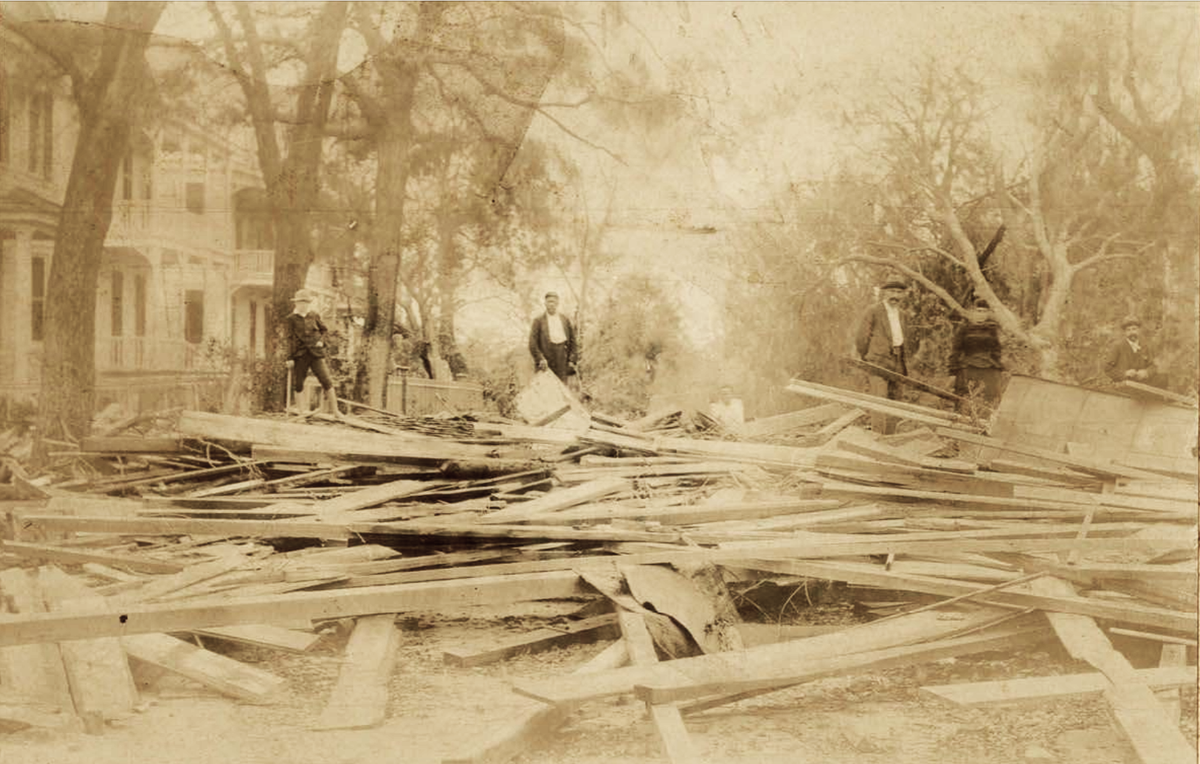 Photograph of people standing in the street amidst hurricane damage. Location: Likely Beaufort, S.C.