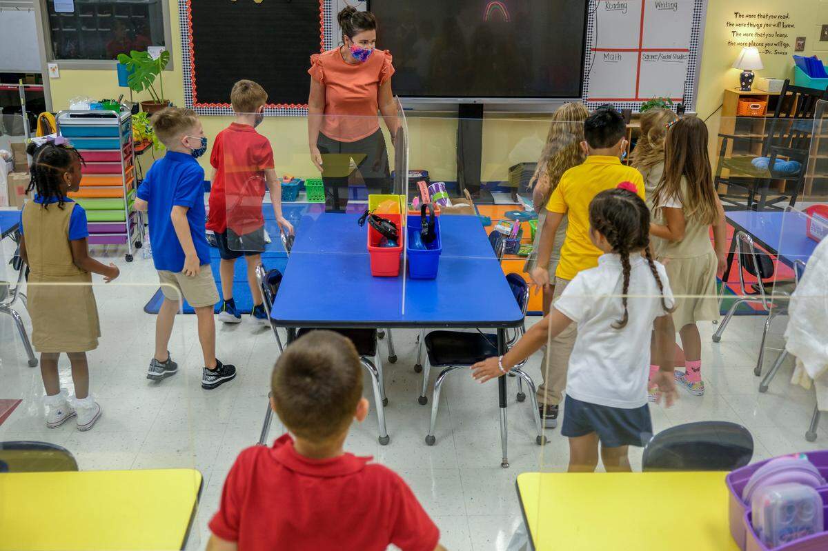 With plexiglass partitions on their desks, first grade students stand on the first day of school to do some stretching exercises, in this instance “the wiggles” led by their teacher Angela McDaniel, top, on Monday, Aug. 16, 2021 at Bluffton Elementary School.
