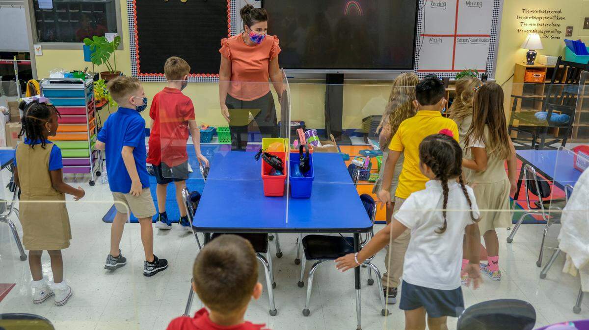 With plexiglass partitions on their desks, first grade students stand on the first day of school to do some stretching exercises, in this instance “the wiggles” led by their teacher Angela McDaniel, top, on Monday, Aug. 16, 2021 at Bluffton Elementary School.