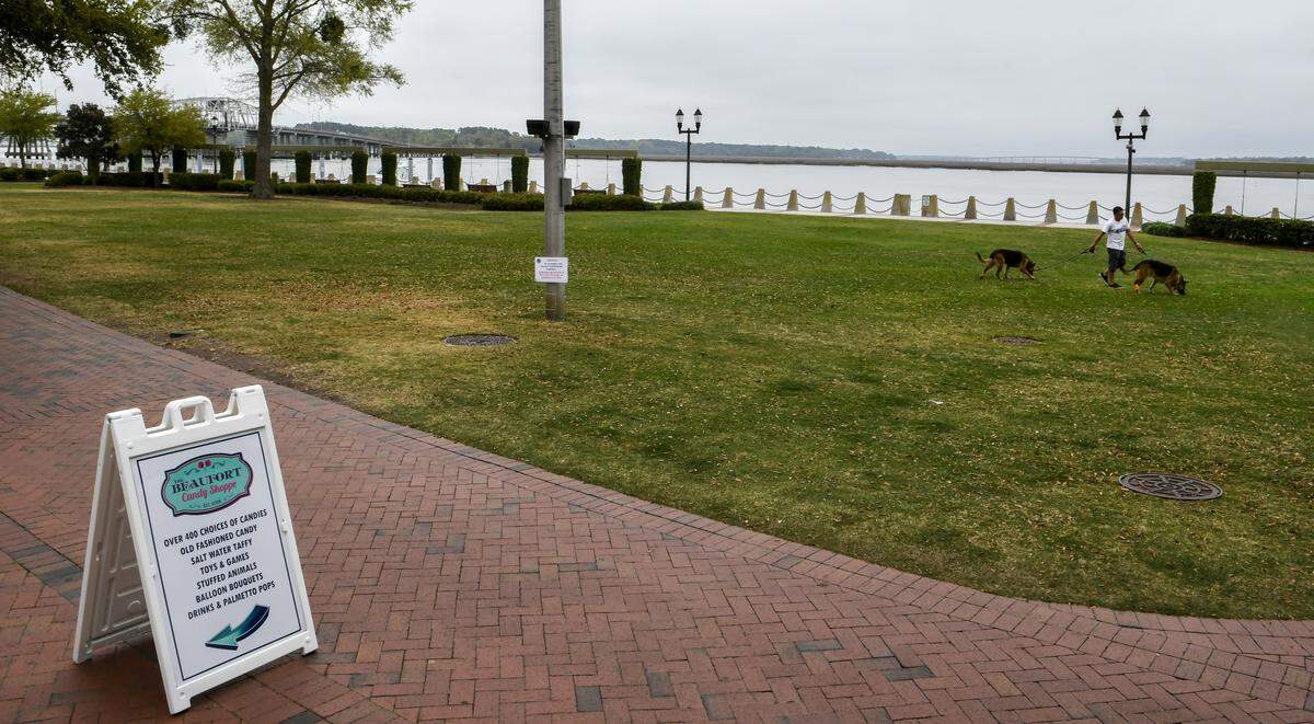 A man walks his dogs in a desolate Henry C. Chambers Waterfront Park on Monday, March 23, 2020, as the coronavirus has turned Beaufort into a ghost town.