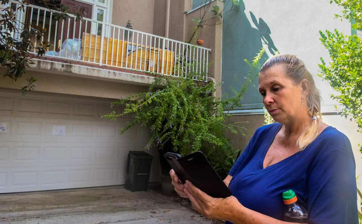 Danielle Smith looks through her phone on Tuesday, Aug. 3, 2022 while standing in the driveway of her Jenkins Island home. On Christmas Eve a burner on her propane-fueled cooktop shot flames into the air incinerating the countertop and the belongings around the open floor-plan kitchen. Behind Smith above the garage on a second-floor deck are fire-damaged goods that Smith’s been told must remain on the premises until insurance inspectors have completed their analysis.