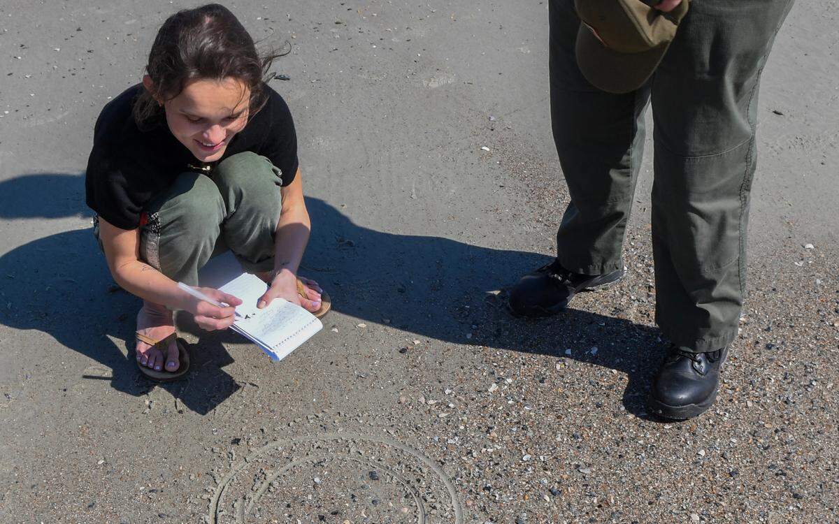 Reporter Sarah Haslehorst finds the smallest of the small shark tooth inside the second ring drawn by S.C. State Park Service Assistant Ranger Candra Workman in March, 2024. The ranger drew a smaller circle that allowed Haselhorst to find the tooth among the other shells and beach debris.