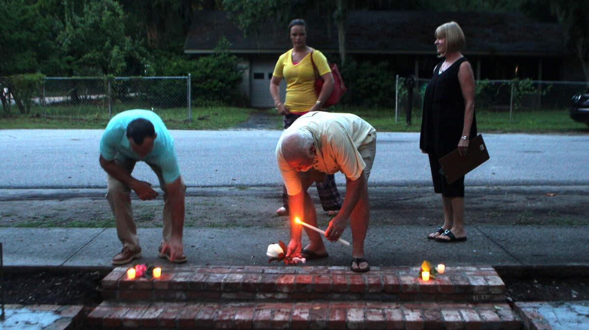 Fred Mix, center, of Bluffton, lays a magnolia flower and his candle at the steps to the home at 80 Calhoun Street during a candlelight vigil on Friday night for the flowers and garden that were recently removed from in front of the Fripp-Lowden House.