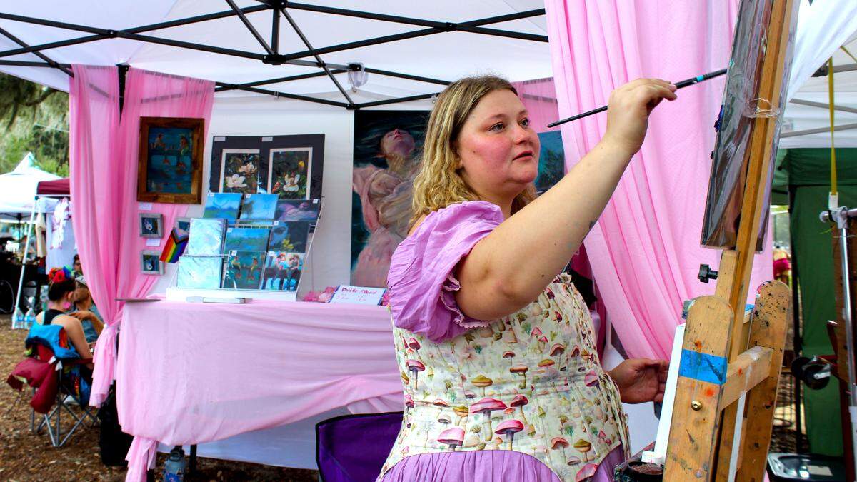Beaufort artist Tatiana Tatum dabs paint on her brush at her stall at Lowcountry Pride Celebration on Oct. 19, 2025. The bisexual artist’s work centers women, often half-submerged in water, or with fishy tails drinking beer by the docks. “Resilience is an important thing for me,” Tatum said. “You don’t drown when people tell you to.”
