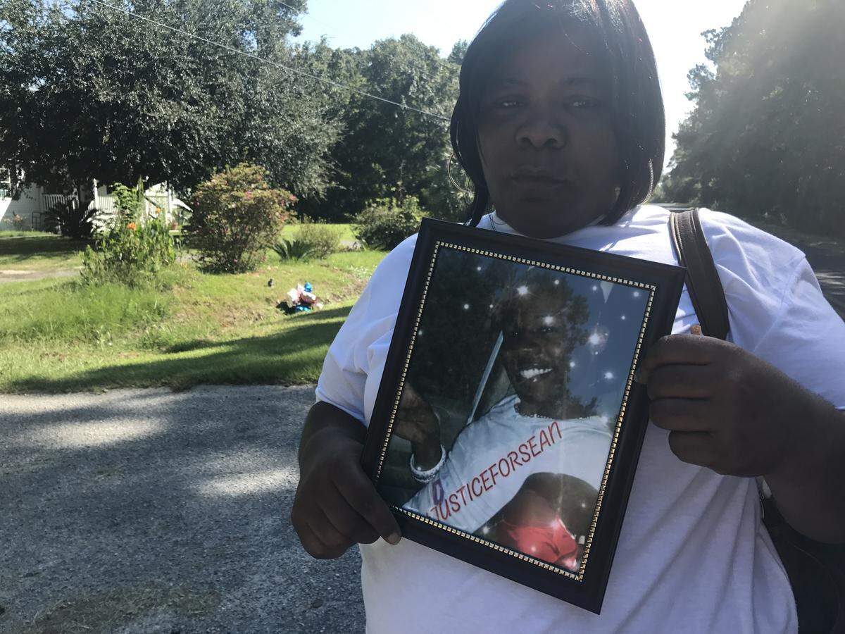 D’Andra Green holds a picture of her son Sean Aiken near the ditch where his body was found.
