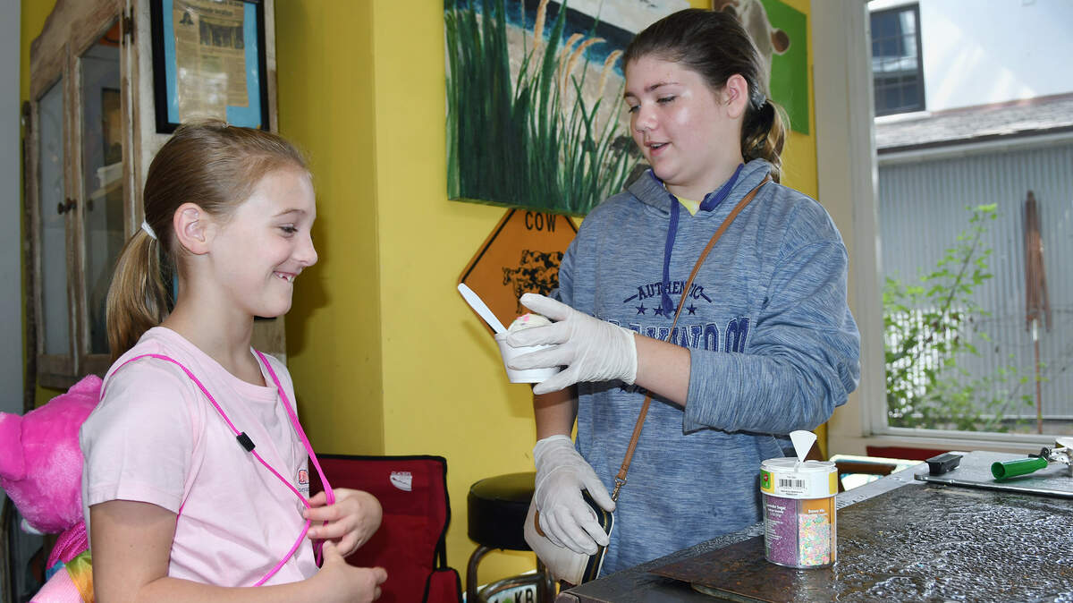 Shelby Pinski, 12, hands a vanilla ice cream with sprinkles to customer Stella Shipman, 8, of Atlanta on Friday at the ice cream stand Pinski has opened in the screened-in porch of Sippin Cow, the Bluffton restaurant owned by her mother, Christy Pinski. Shelby said she opened the stand — which she is calling “Udderly Good” until she can think up a better name — to raise money for a cat and a car to drive when she turns 16.