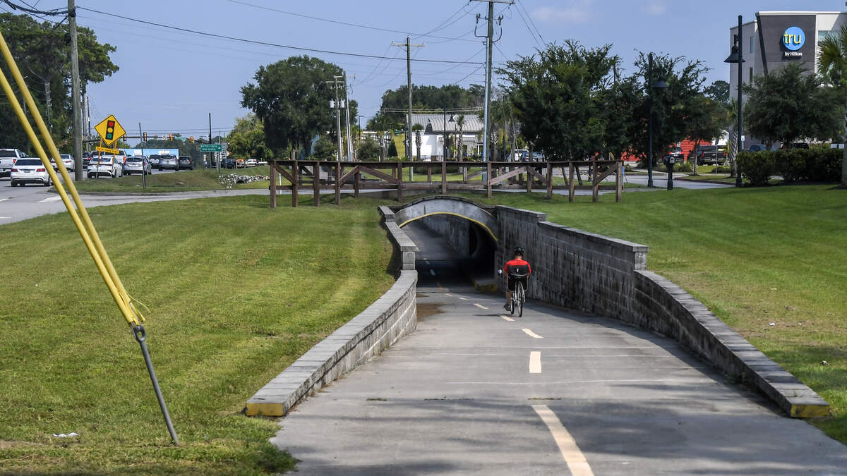 A on Aug. 22, 2025, a bicyclist goes through a tunnel, controversial at the time of construction, for the Spanish Moss Trail which keeps users safe from vehicles turning off Trask Parkway (U.S. 21) into an area with several hotels.