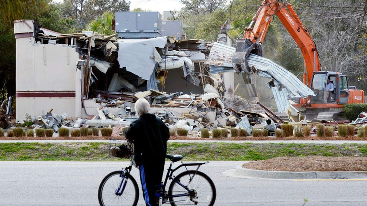A bicyclist pauses to watch the as the demolition  of the old Smokehouse restaurant proceeds on Tuesday afternoon on Hilton  Head Island. The restaurant along Pope Avenue near Coligny Circle, was  most recently used as a temporary fire station by the Town of Hilton  Head Island.