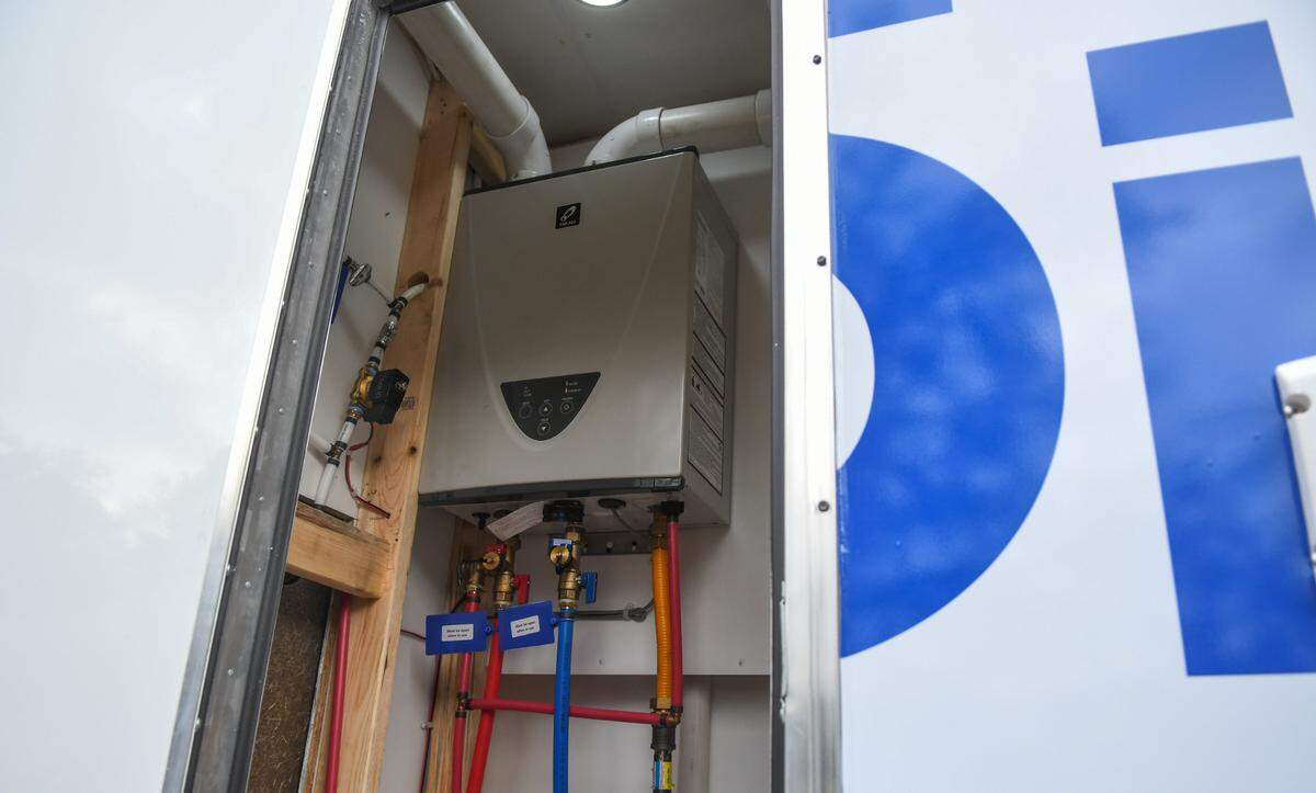 A tankless water heater sits on one side of the 24-foot trailer that is equipped with a 400 gallon water tank that has two full bathrooms and a stackable washer and dryer for laundry.