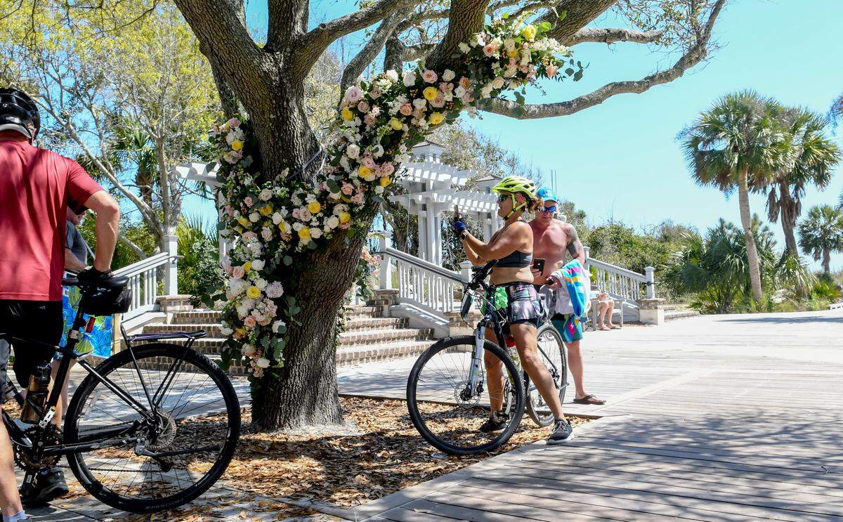 Bikers and beachgoers stop to take pictures of floral arrangements wrapped around a live oak on Friday, March 20, 2020 at Coligny Beach Park on Hilton Head Island just minutes before Hilton Head Mayor John McCann closed the beach and the park’s facilities due to the COVID-19 virus. The arrangements, designed by Jardiniere Events Extraordinaire, were donated by brides who canceled their weddings because of the coronavirus. The event planner called it a “flower flash.”