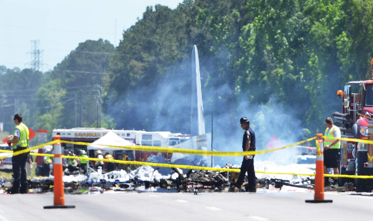 Officials investigate the scene of a C-130 military carg plane crash that happened on Wednesday on Ga. 21 near Savannah-Hilton Head International Airport. Part of the tailplane of the aircraft can be seen rising in the center left portion of the frame. The plane went down on the road near its intersection with Crossgate Road.