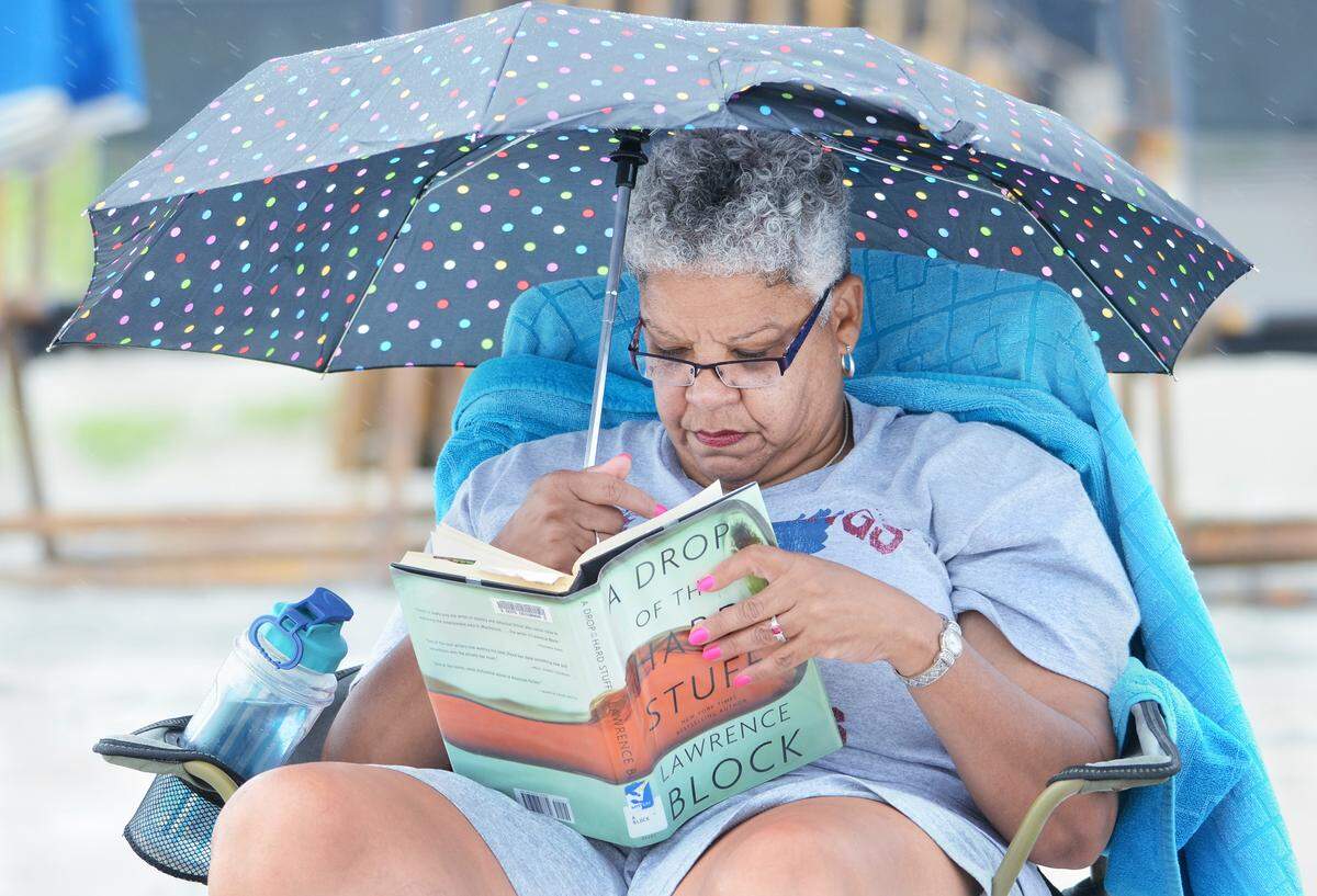 Vacationer Deborah Barksdale, of Atlanta, uses her polkadot umbrella to keep the raindrops from falling on her detective novel, "A Drop of the Hard Stuff," by Lawrence Block, while reading at Coligny Beach Park on Monday. "I'm hoping for some sunshine while I'm here, but that's OK, the beach is always nice," she said, "Call it heaven, rain or shine." 