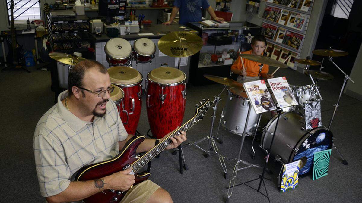 Mike Ponder, co-owner of the newly opened B-Sharp Music Store, tries out a Schecter C1 Plus electric guitar while son Jarrod, 10, plays the drums and fellow owner Jeremy Haden mans the register Friday afternoon in Beaufort.