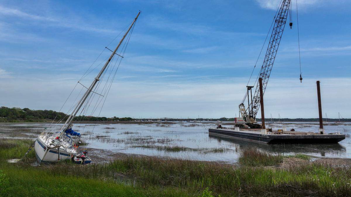 As the tide came in on the evening of April 23, 2025, workers with O’Quinn Marine pushed this barge and crane into the tidal marsh of the Beaufort River in Historic Beaufort. The crane will be used to remove three sailboats, including the one pictured, that were ripped from their moorings after Tropical Storm Helene in 2024.