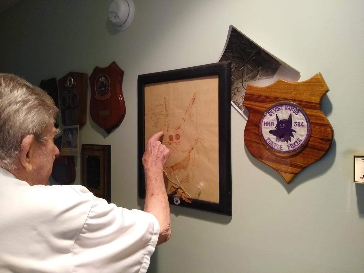 Col. Joseph R. Dobbratz Jr. points to a sketch of Swifty, the mascot of Marine Medium Helicopter Squadron 364, known as the “Purple Foxes.” Dobbratz served as the squadron’s commanding officer for six months while deployed in Vietnam in 1968. The glass on the frame is cracked where a piece of shrapnel impaled it during a rocket strike.