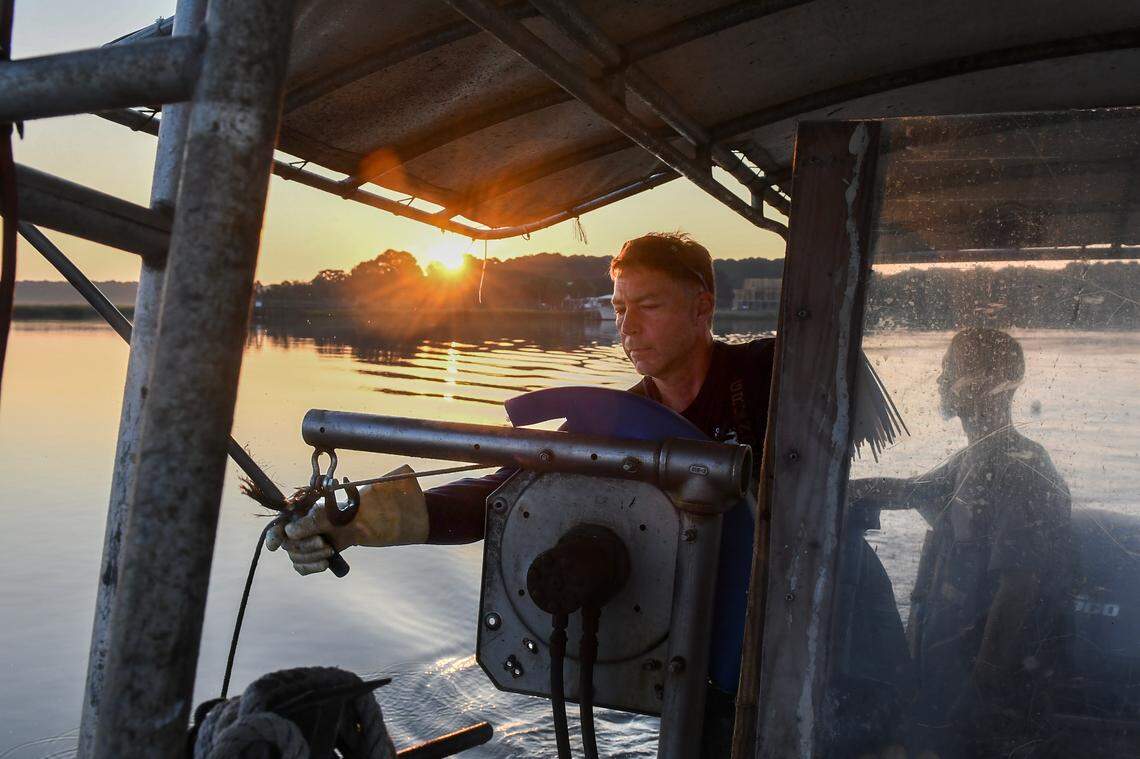 After using a pole to snag the line of one of his crab pots, Brett Everett, center, owner of Rusty Crabs, uses a winch to drag the pot to the surface on the morning of Sept. 20, 2024, in the waters off St. Helena Island.