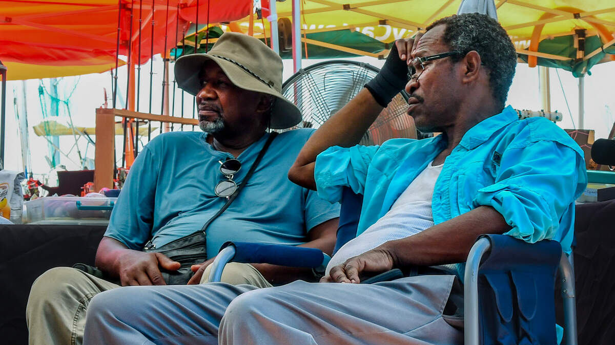 Columbia, S.C. based gems and rocks artist Allen Gibbs, left, and next-door neighbor Florida-based sculptor Byron Lawrence sit under Gibbs’ tent on July 20, 2023 at Henry C. Chambers Waterfront Park as numerous fans circulate the air at the Beaufort Water Festival. With feel-like temperatures soaring above 110s°F, Gibbs brought a small, portable air conditioning unit but couldn’t get the fan to work faster. “The buttons are so tiny it’s hard to see how to turn it up” he said as the two chatted, waiting for customers.