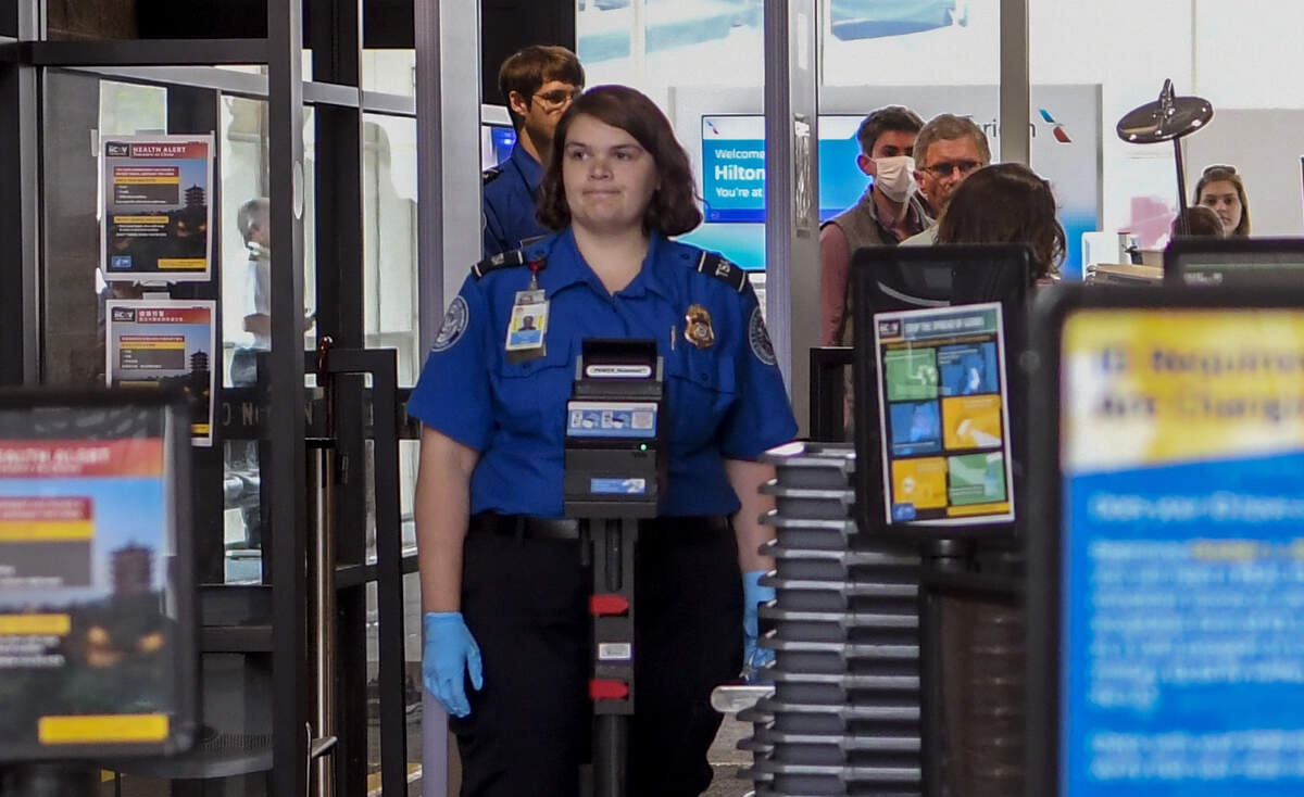 A Transportation Security Administration agent waits for additional ticket holders at Hilton Head Airport on the morning of Friday, March 27, 2020, as people, many of which wore masks and gloves for personal protection, wait for their carry on baggage to be checked.