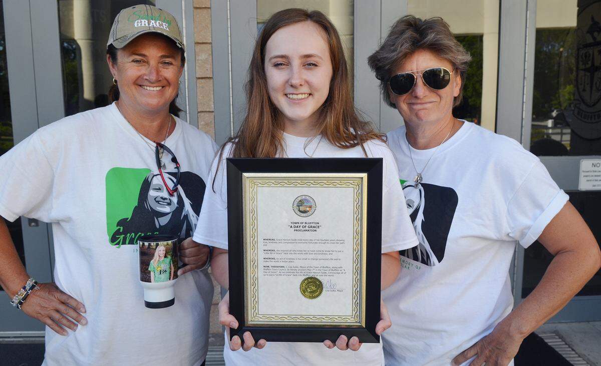 Grace Sulak’s mothers, Heidi Hanson, left, and Kristen Sulak, right, and Grace’s twin sister, Faith, are photographed with a proclamation from the Town of Bluffton making May 7 “A Day of Grace.”