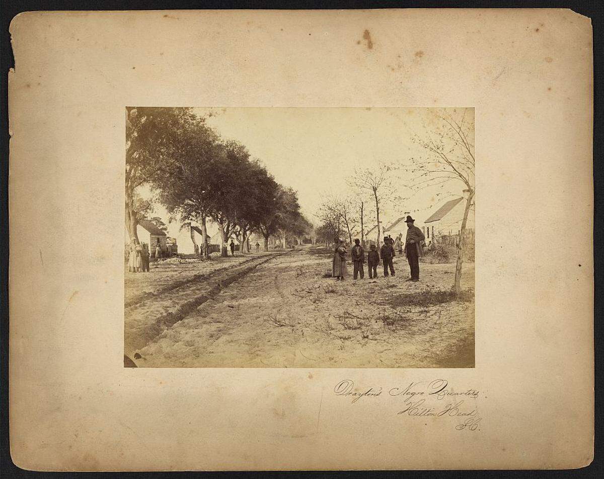 Enslaved people stand outside slave quarters on Drayton’s Fish Haul plantation, located near present day Mitchelville and Port Royal Plantation.