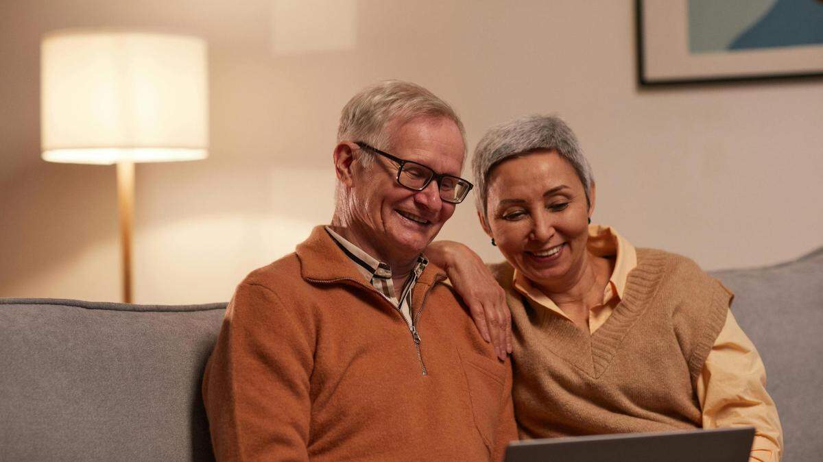 An elderly couple sit at home on the couch