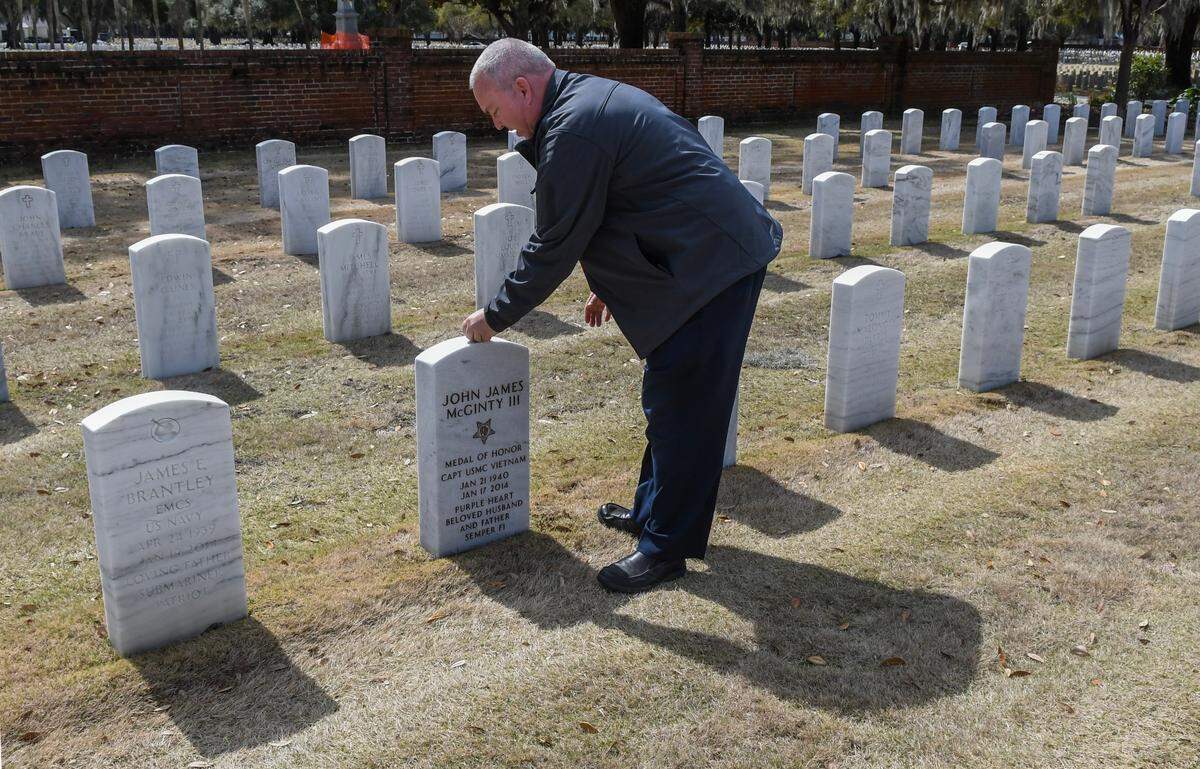 Michael Brophy, assistant director of the Beaufort National Cemetery, replaces a nickel on top of the grave marker for Medal of Honor recipient John James McGinty, III on Monday, March 3, 2025, in Beaufort. According to the Montana Department of Military Affairs, a penny means a person visited. A nickel means they trained together at boot camp. A dime means they served together and a quarter signifies the visitor was with the veteran when they died.